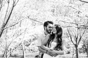 A couple embraces and laughs together in a romantic black and white moment under blooming spring trees.