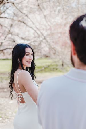 A romantic photoshoot under blooming cherry blossom trees with a couple in white outfits on a spring day.