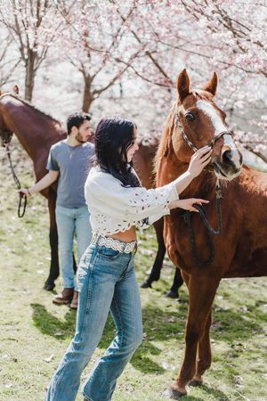 Candid moments with a couple and their horse under flowering trees during a spring photoshoot.