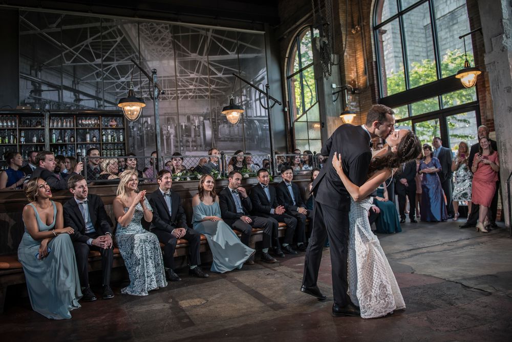 A couple shares their first dance at a rustic barn wedding reception surrounded by seated guests.