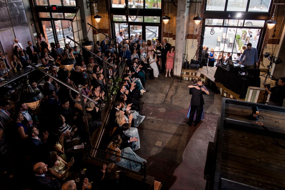 Wedding reception celebration in a rustic indoor venue with wooden beams and warm lighting.