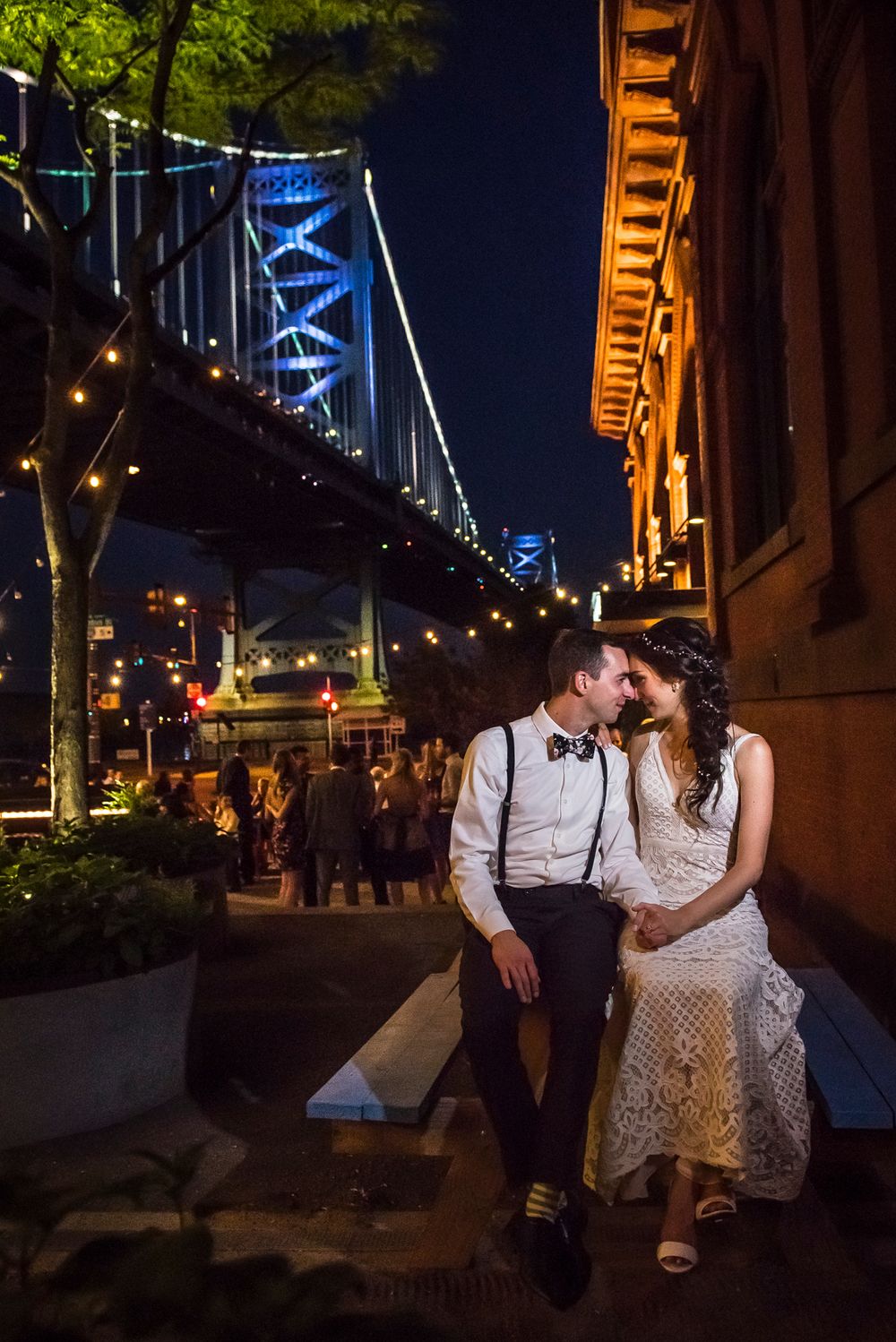 A romantic evening scene with a couple sitting together under decorative blue lights and string lighting in an urban setting.