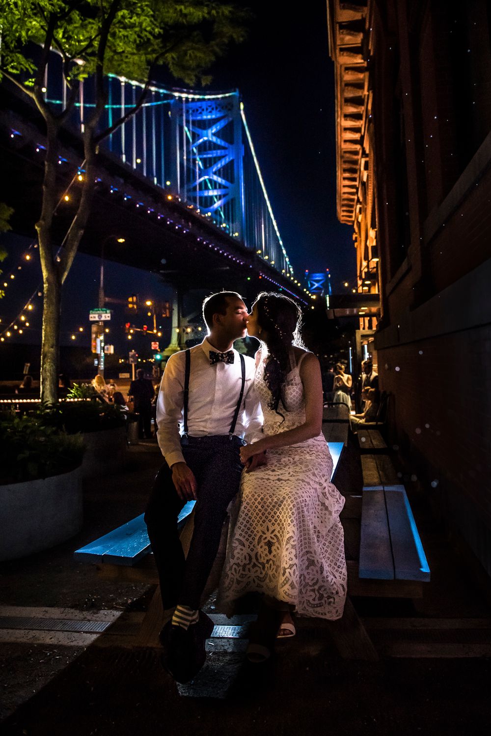 A couple dances together at an outdoor evening celebration decorated with blue lights and string lighting.
