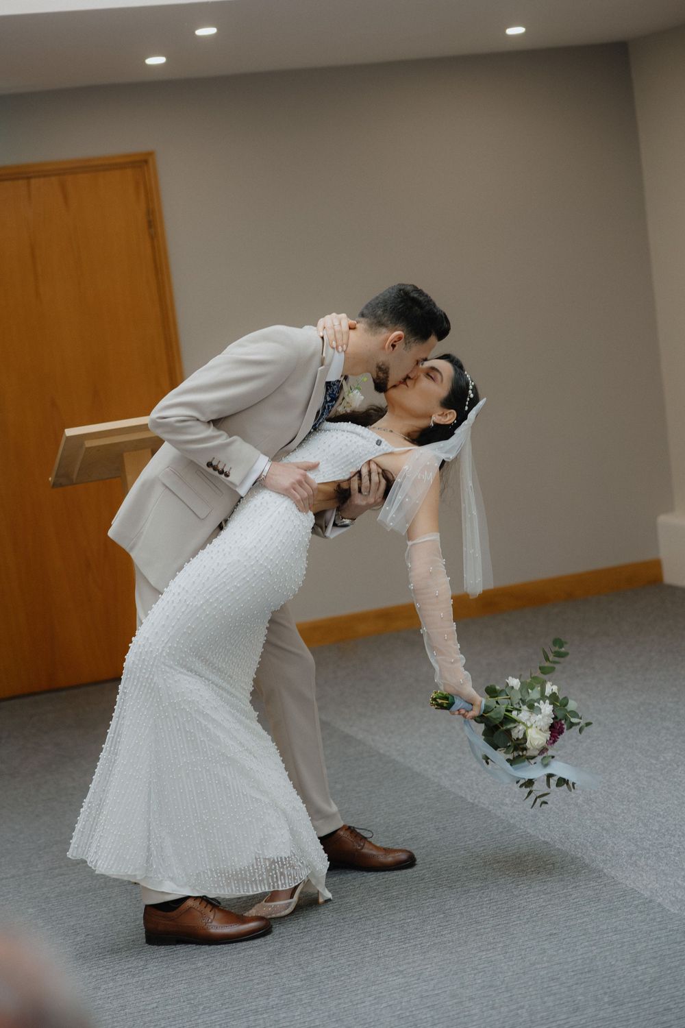 A romantic dip kiss between newlyweds, with the bride holding a floral bouquet.