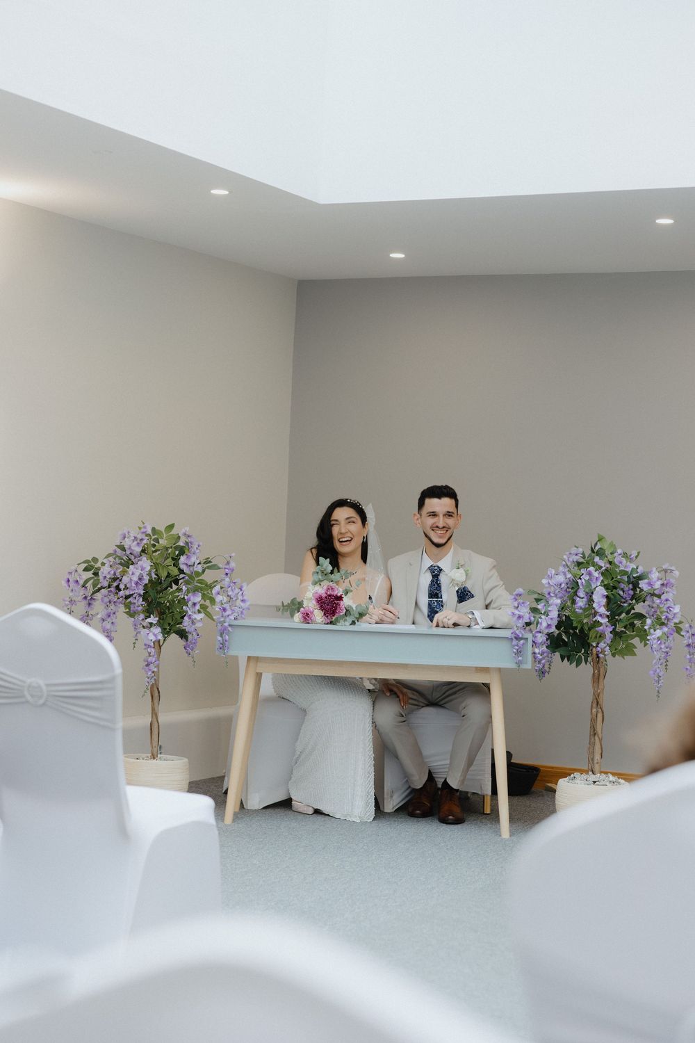 Modern minimalist wedding reception setup with purple floral centerpieces and white chairs.