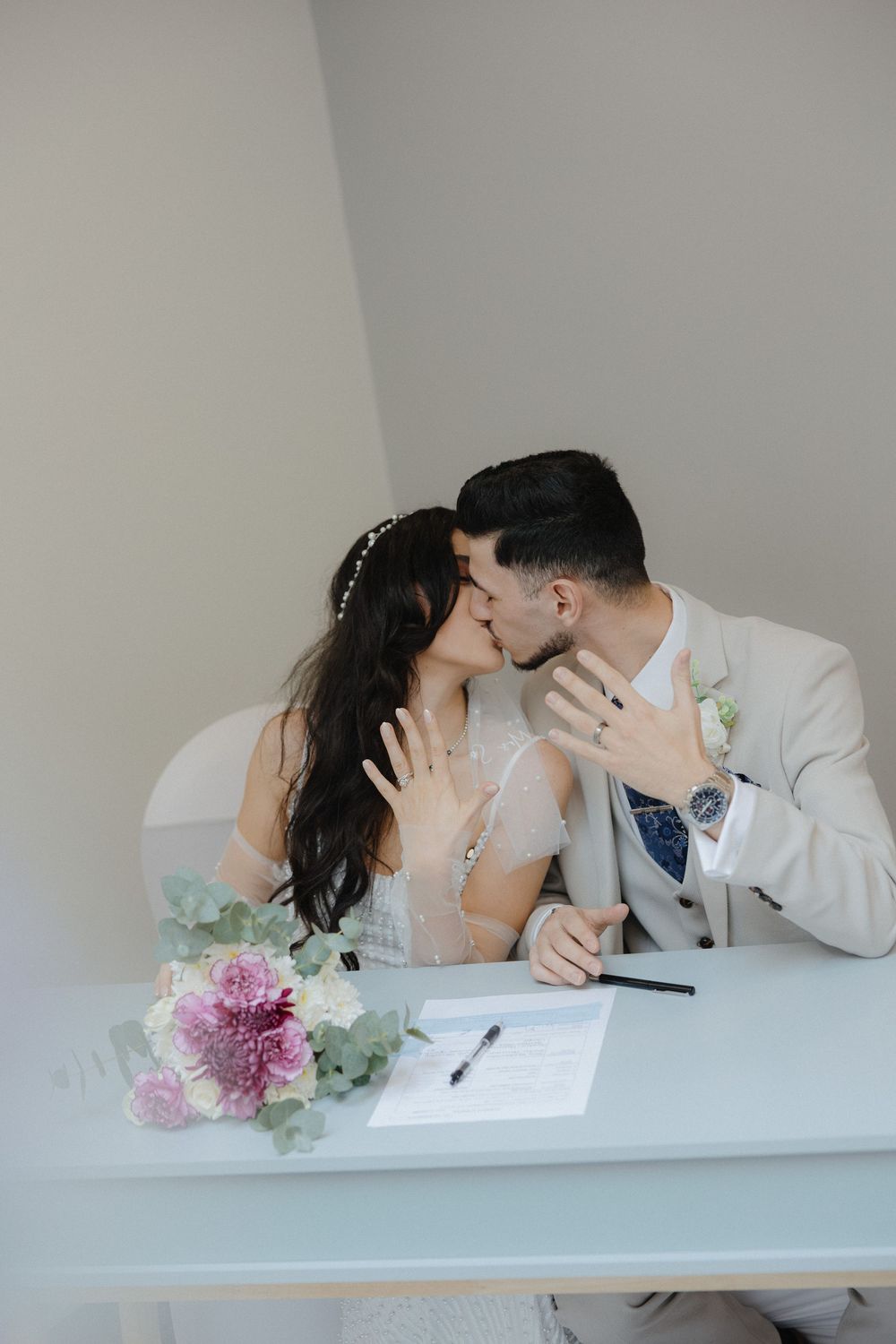 Couple signing marriage documents with floral decorations on a white table.