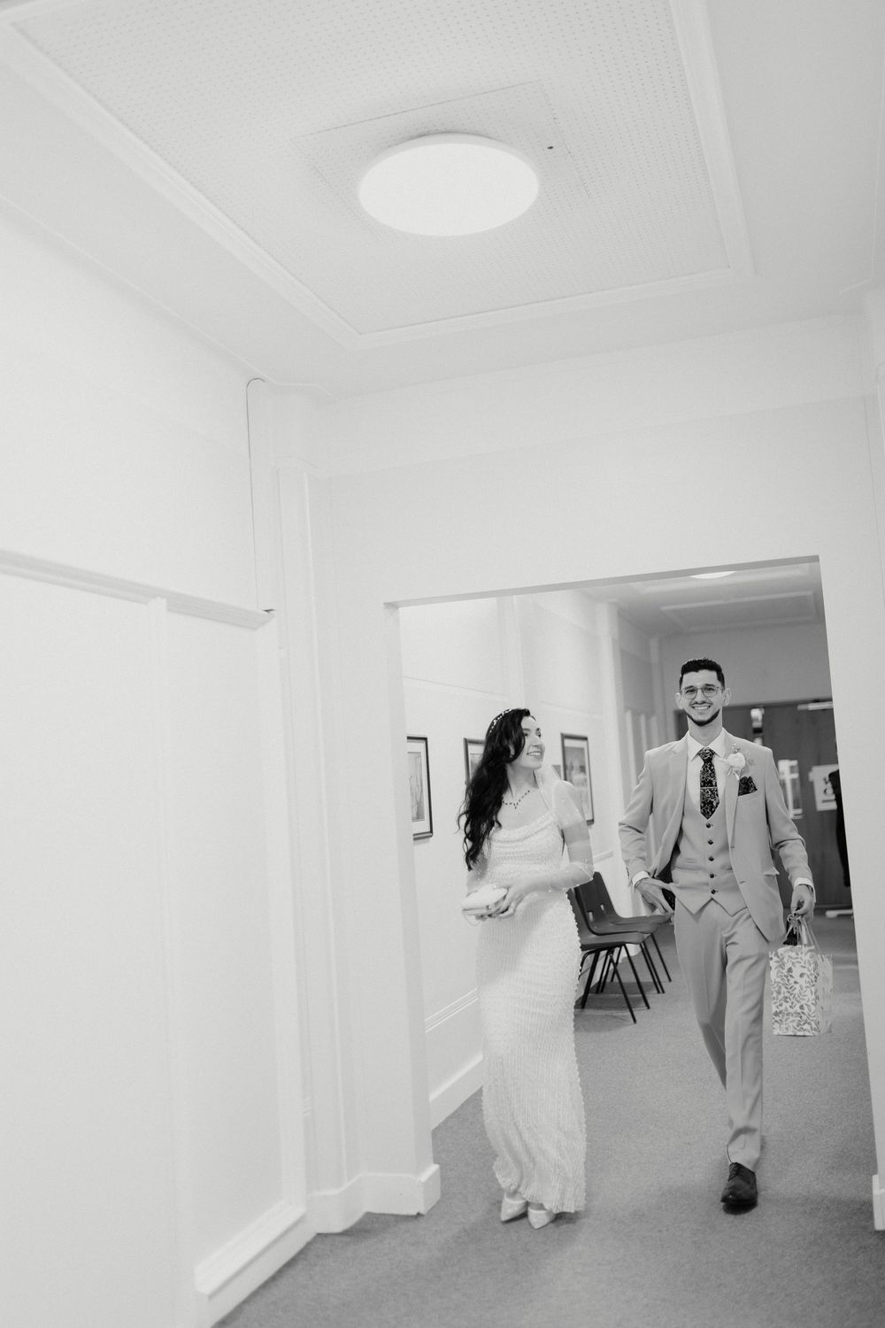 A minimalist white hallway with natural light showing people walking through during a wedding ceremony.