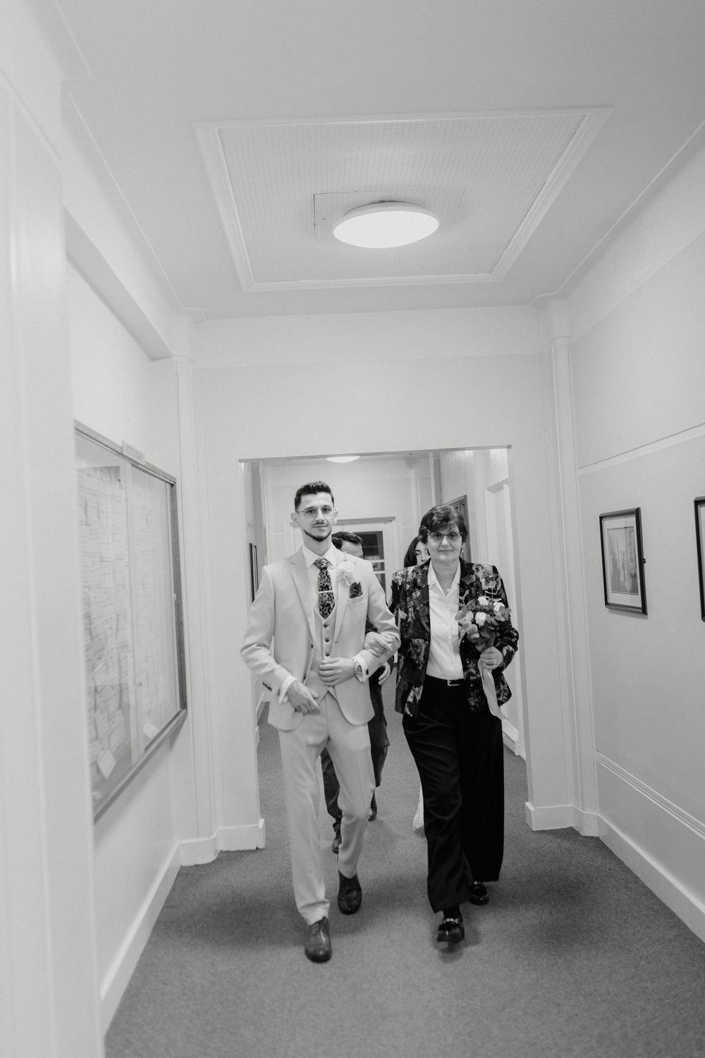Two people walking down a hallway in formal attire, captured in black and white photography.