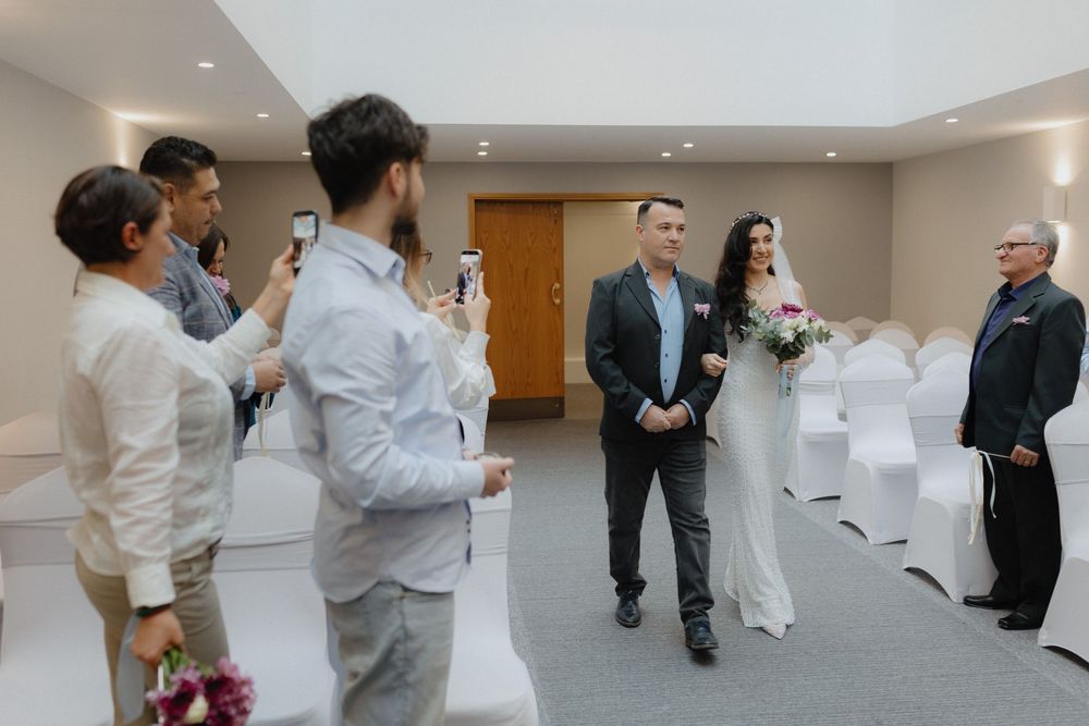 A wedding ceremony in progress in a modern indoor venue with white chairs and guests in attendance.