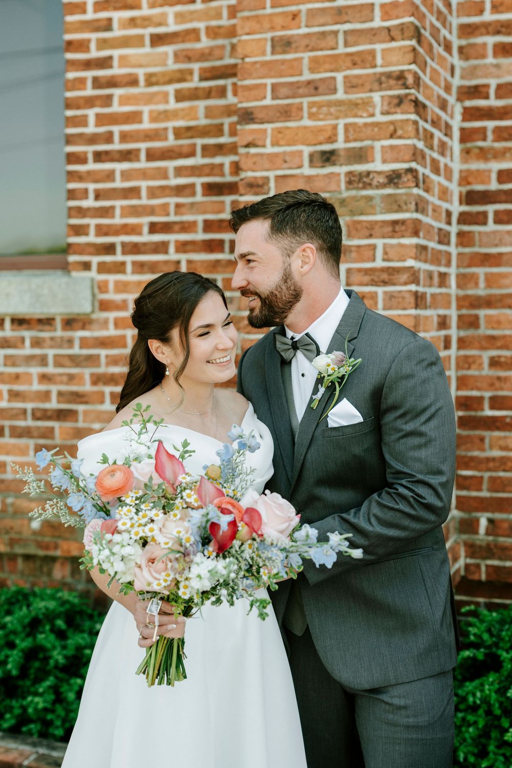 A romantic wedding portrait series showing tender moments against a brick wall with a beautiful floral bouquet.