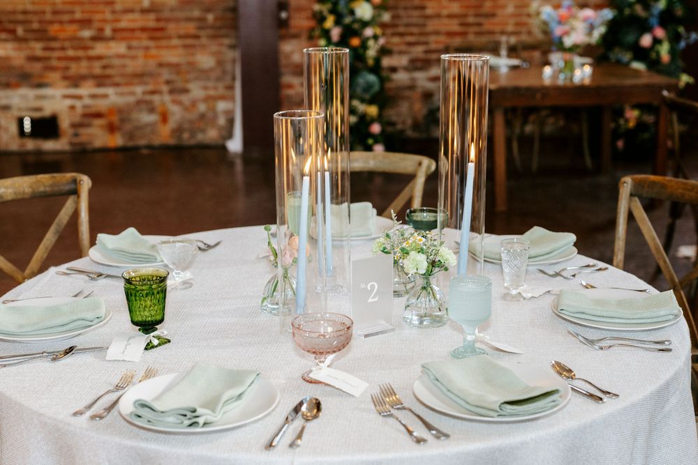 Wedding reception table settings with candles and floral centerpieces arranged against exposed brick walls.