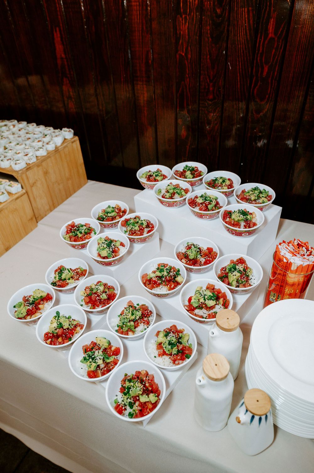 Multiple white bowls filled with fresh salads featuring tomatoes and greens arranged on a white tablecloth for catering service.