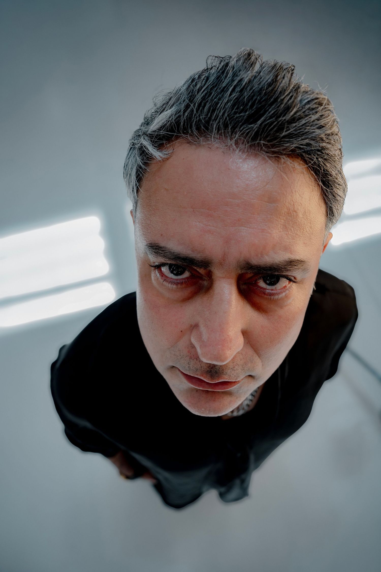 Dramatic wide-angle portrait shot from above showing person in black clothing against white floor.