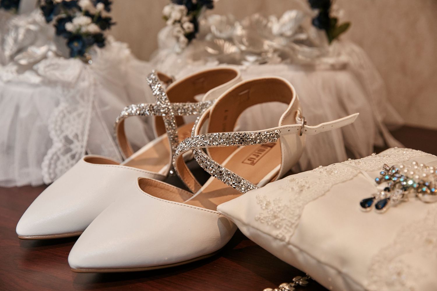 Elegant white satin bridal shoes with delicate crystal embellishments displayed on a rustic wooden surface.