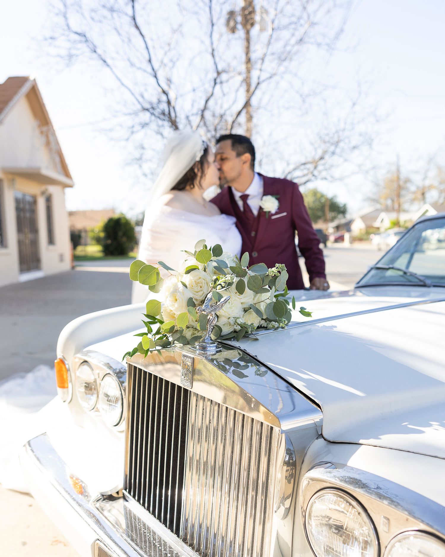 A classic white Rolls Royce decorated with elegant floral arrangements sits parked for a wedding celebration.