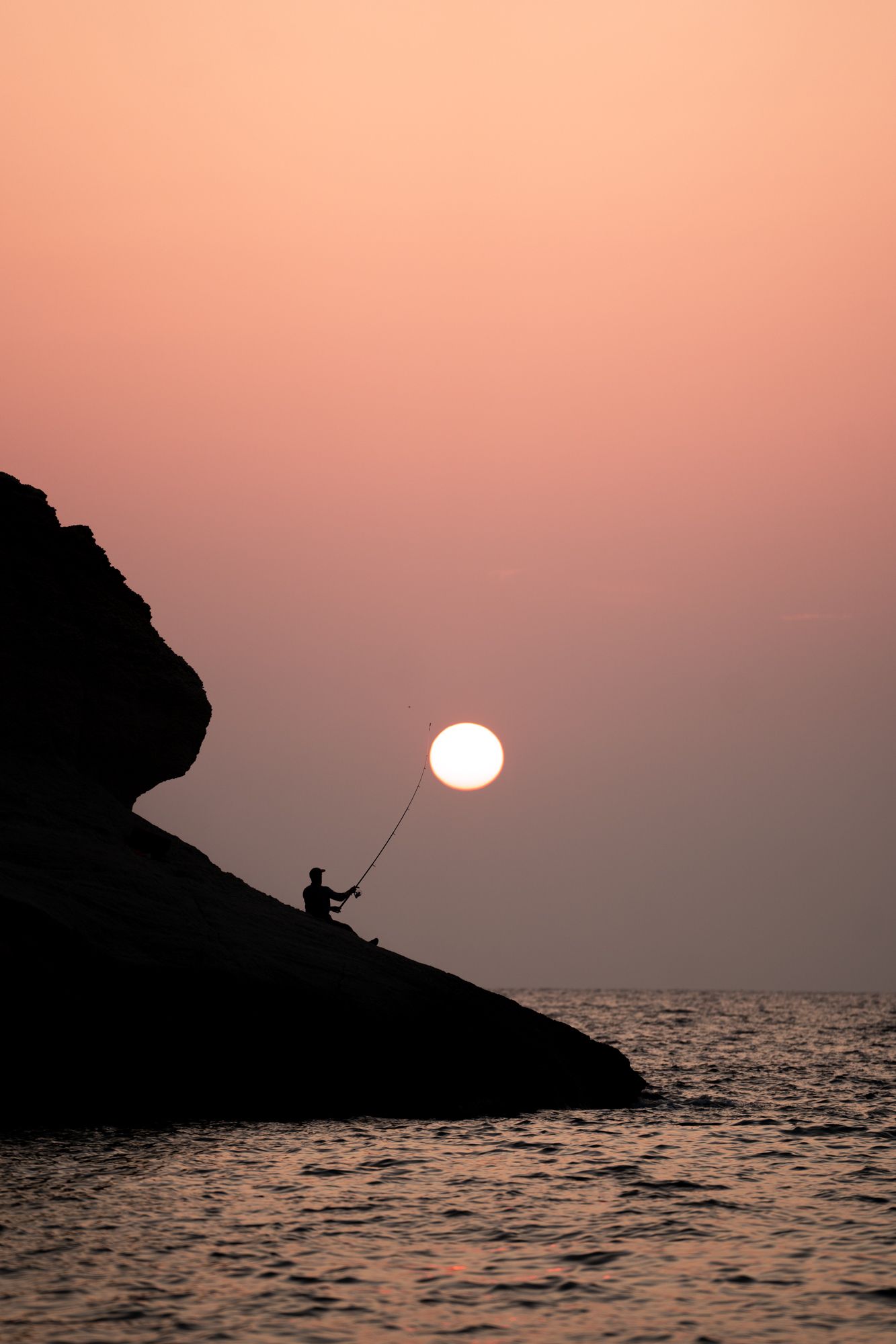 coucher de soleil sur une falaise au-dessus de la mer avec un pêcheur
