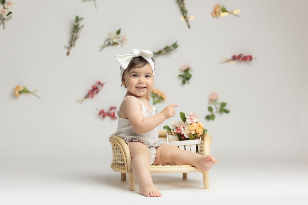 A smiling baby sitting on a wooden chair and playing with toys.