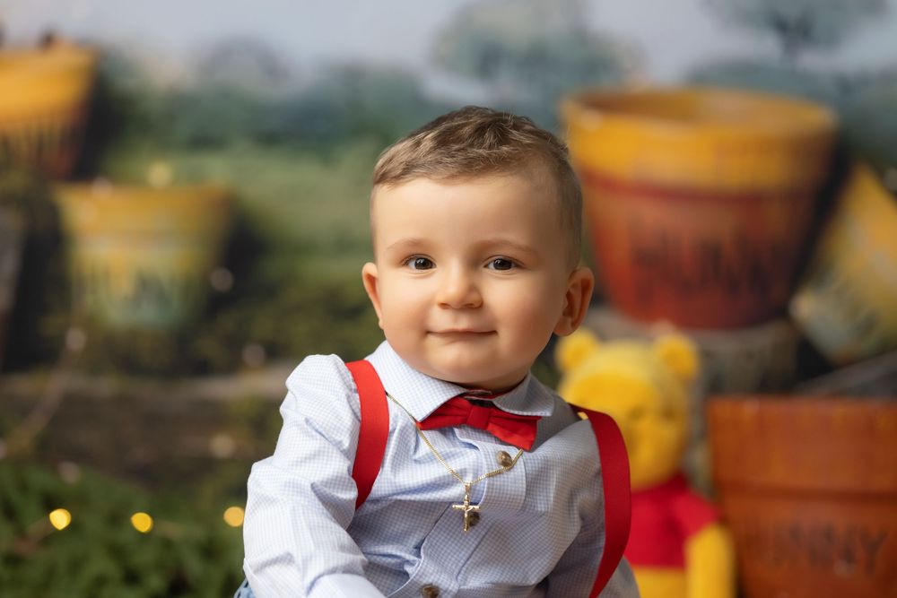 A young boy with blond hair wearing a red bowtie and white shirt smiles happily in a garden setting.