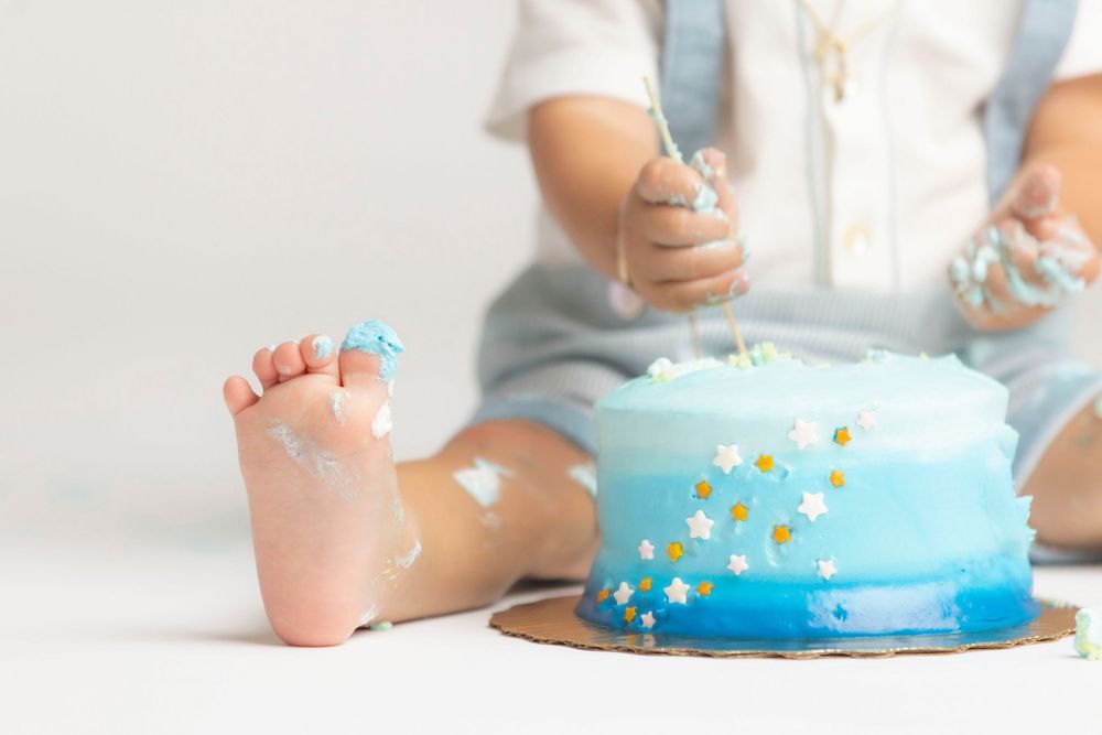 A close-up view of a baby's feet next to a blue and yellow birthday cake.