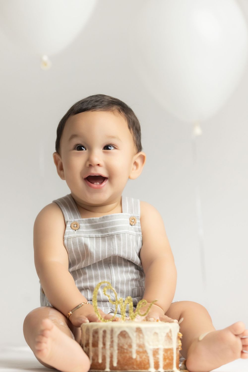 A smiling baby sitting on a white background, wearing a striped outfit and looking directly at the camera.