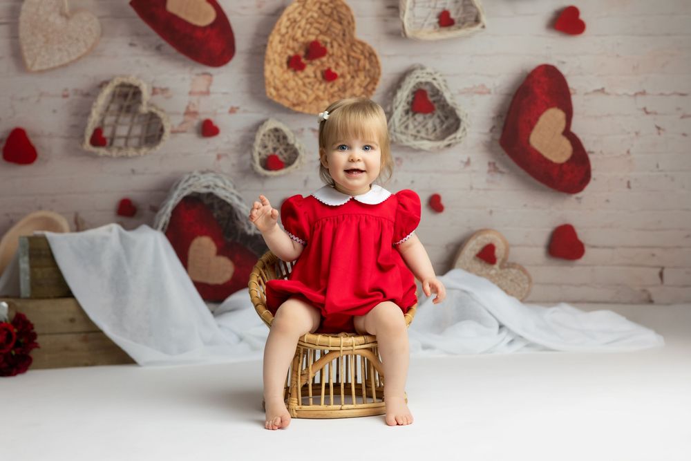 A young girl wearing a red dress sits on a wooden crate surrounded by heart-shaped decorations.