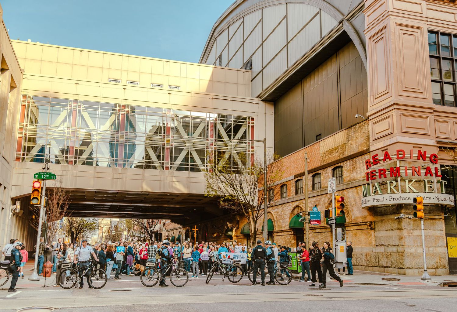 Crowd of cyclists and pedestrians gather outside Reading Terminal Market in Philadelphia on a sunny day.