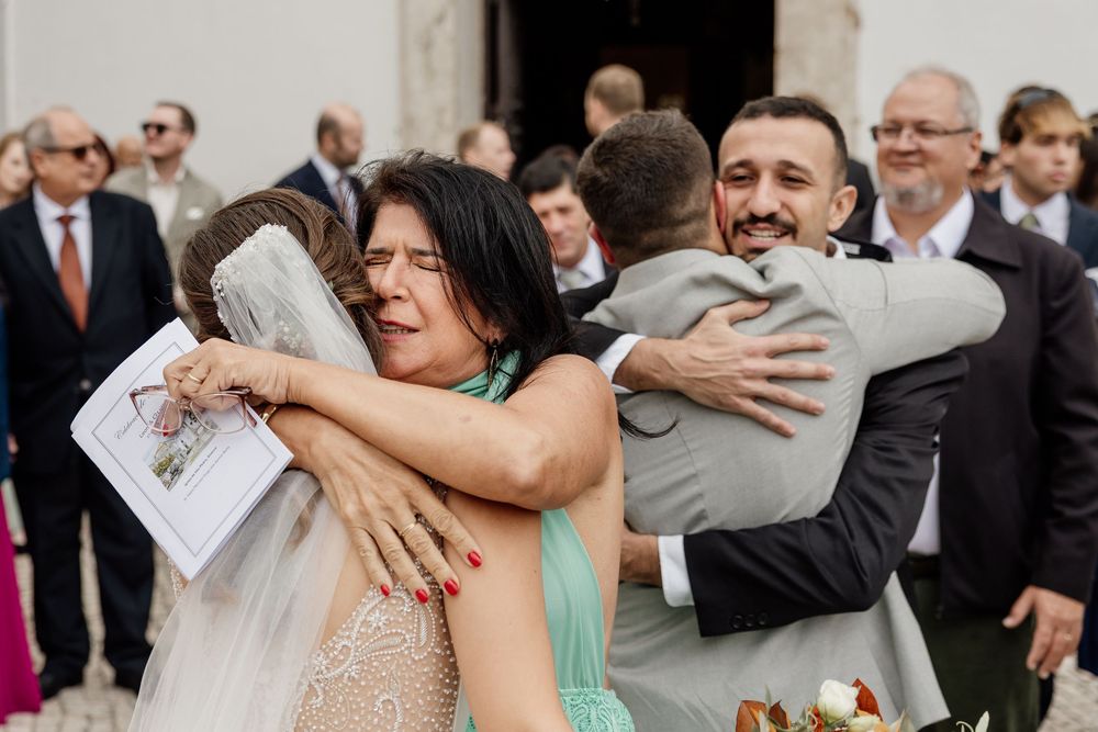 Emotional wedding guests sharing heartfelt hugs outside a church, with tearful embraces captured in a candid moment.