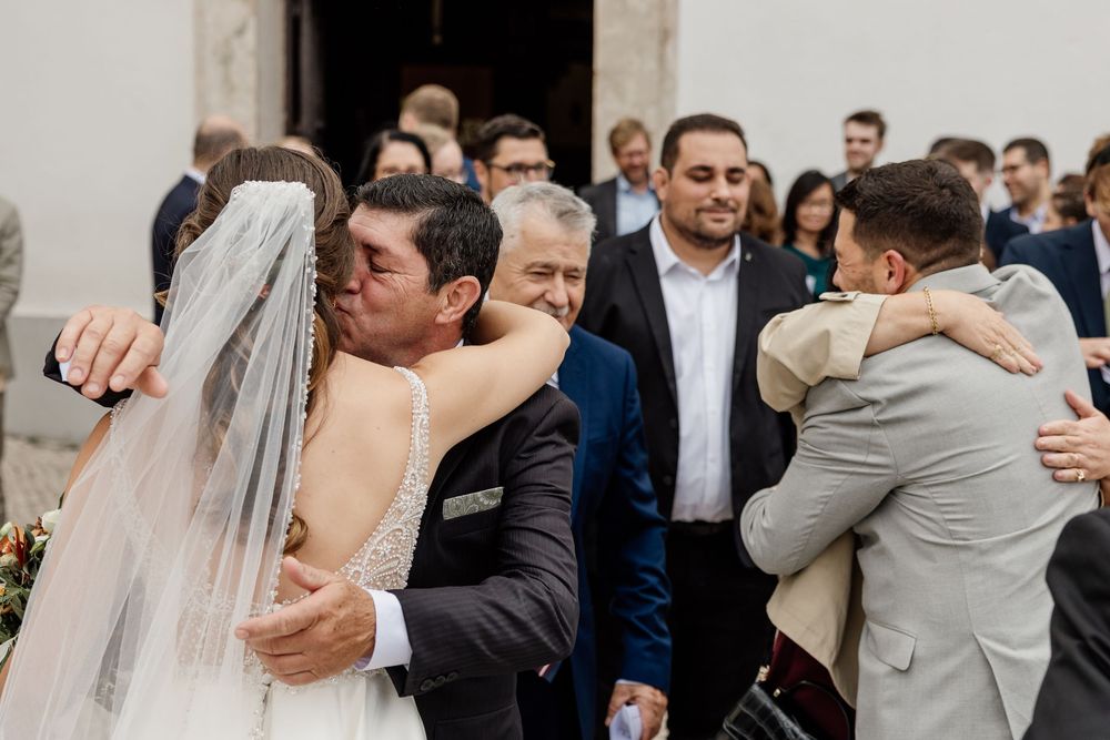 Bride and groom share emotional hugs with guests outside a church after their wedding ceremony.
