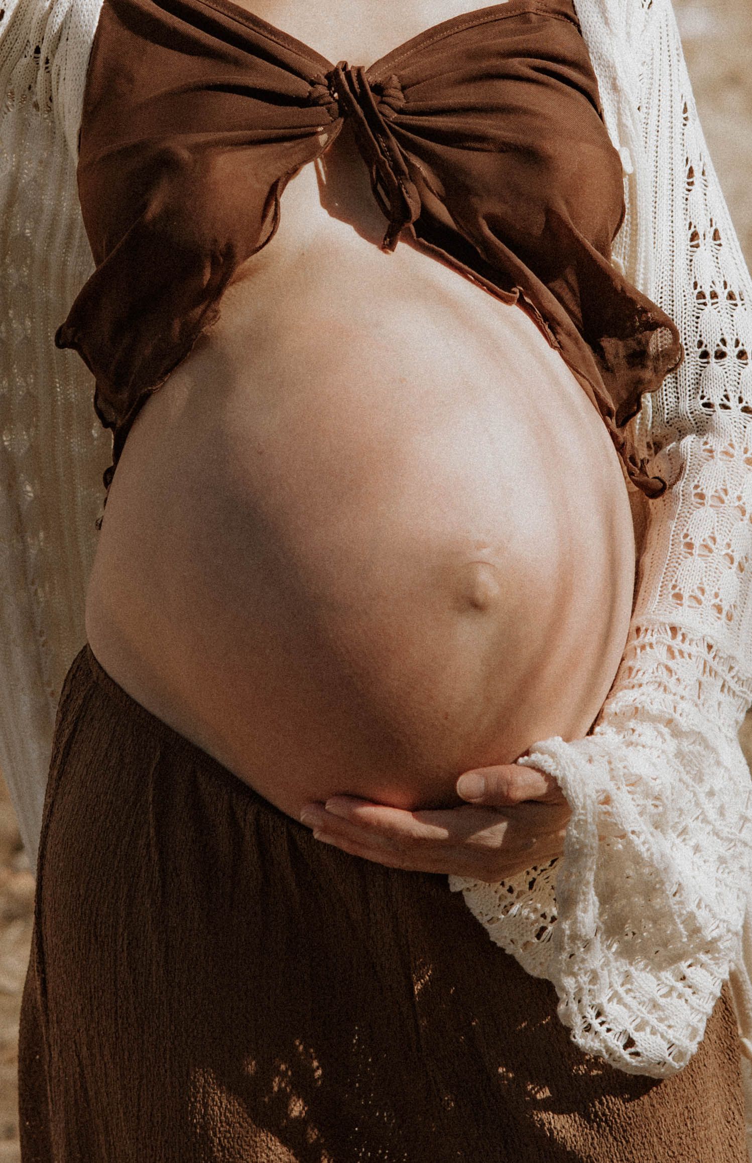 gravid kvinna står och håller om sin mage. på sig har hon en ljus klänning med ett hål för magen.