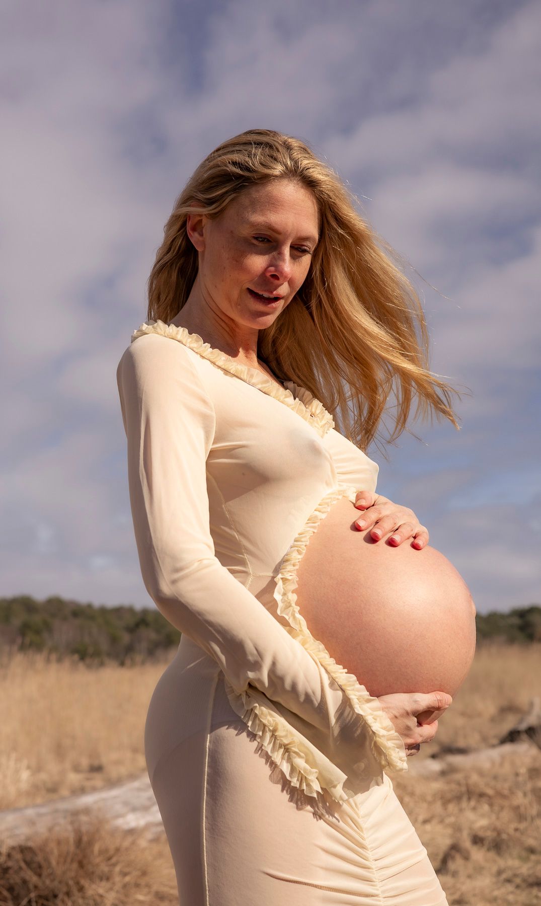 gravid kvinna står och håller om sin mage. på sig har hon en ljus klänning med ett hål för magen.