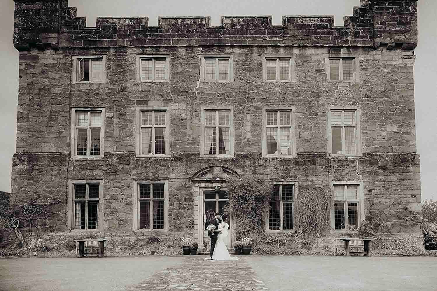 A couple stands at the entrance of a grand stone castle with ivy-covered walls and historic Georgian windows at Askham Hall