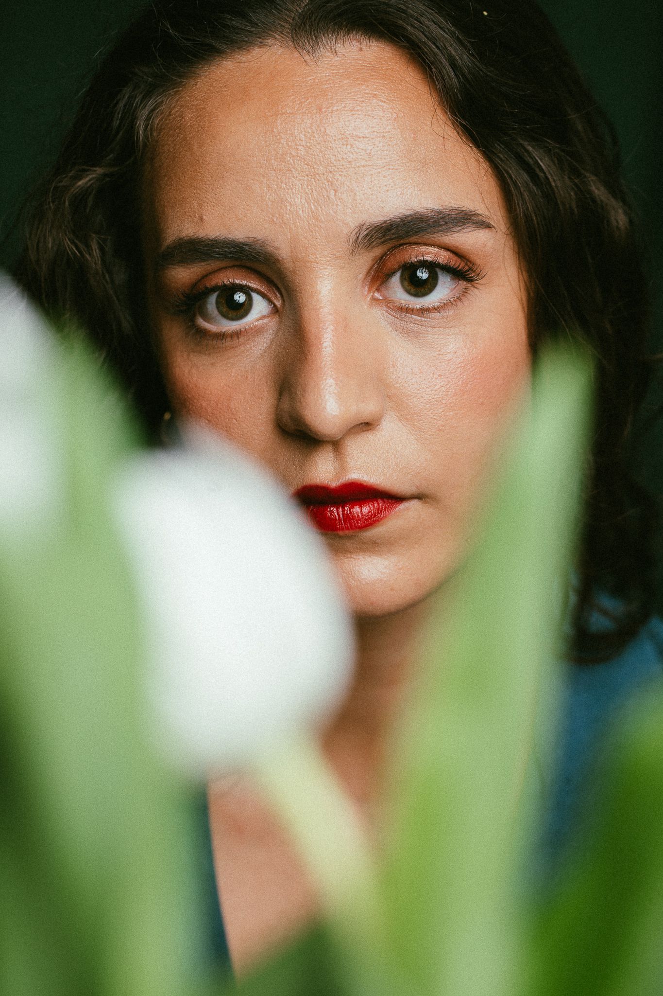 Artistic portrait through foliage showing red lipstick and dramatic lighting with a blurred green foreground.