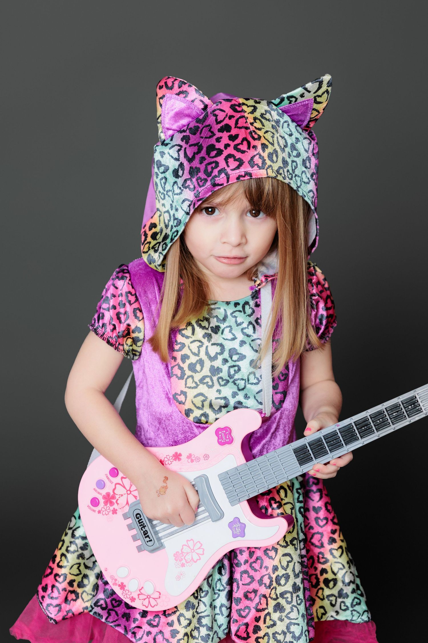 A colorful leopard print dress and cat ear outfit is paired with a pink toy guitar against a dark background.