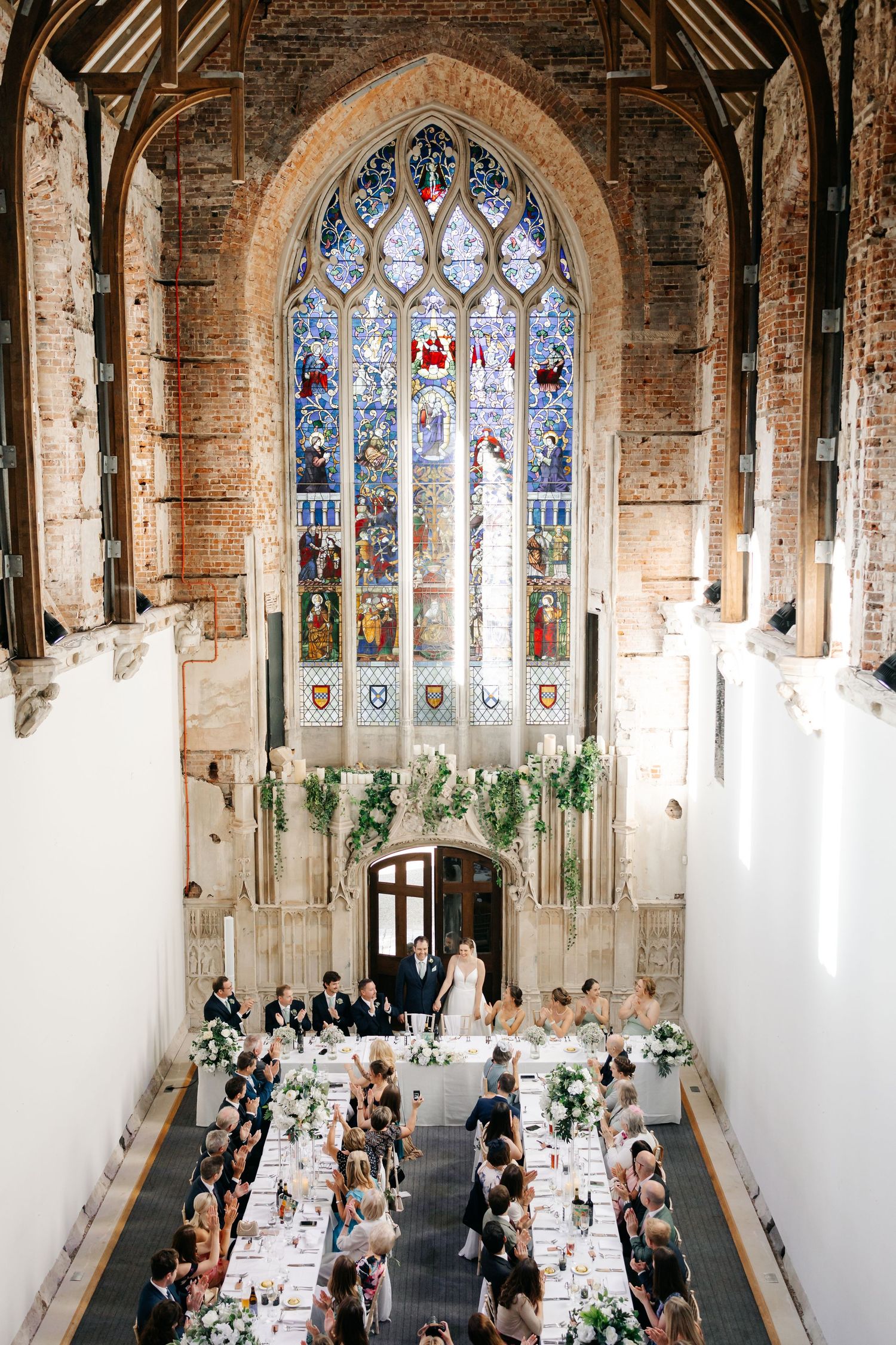Elegant white wedding venue interior with wooden beams and columns featuring rows of light-colored chiavari chairs.
