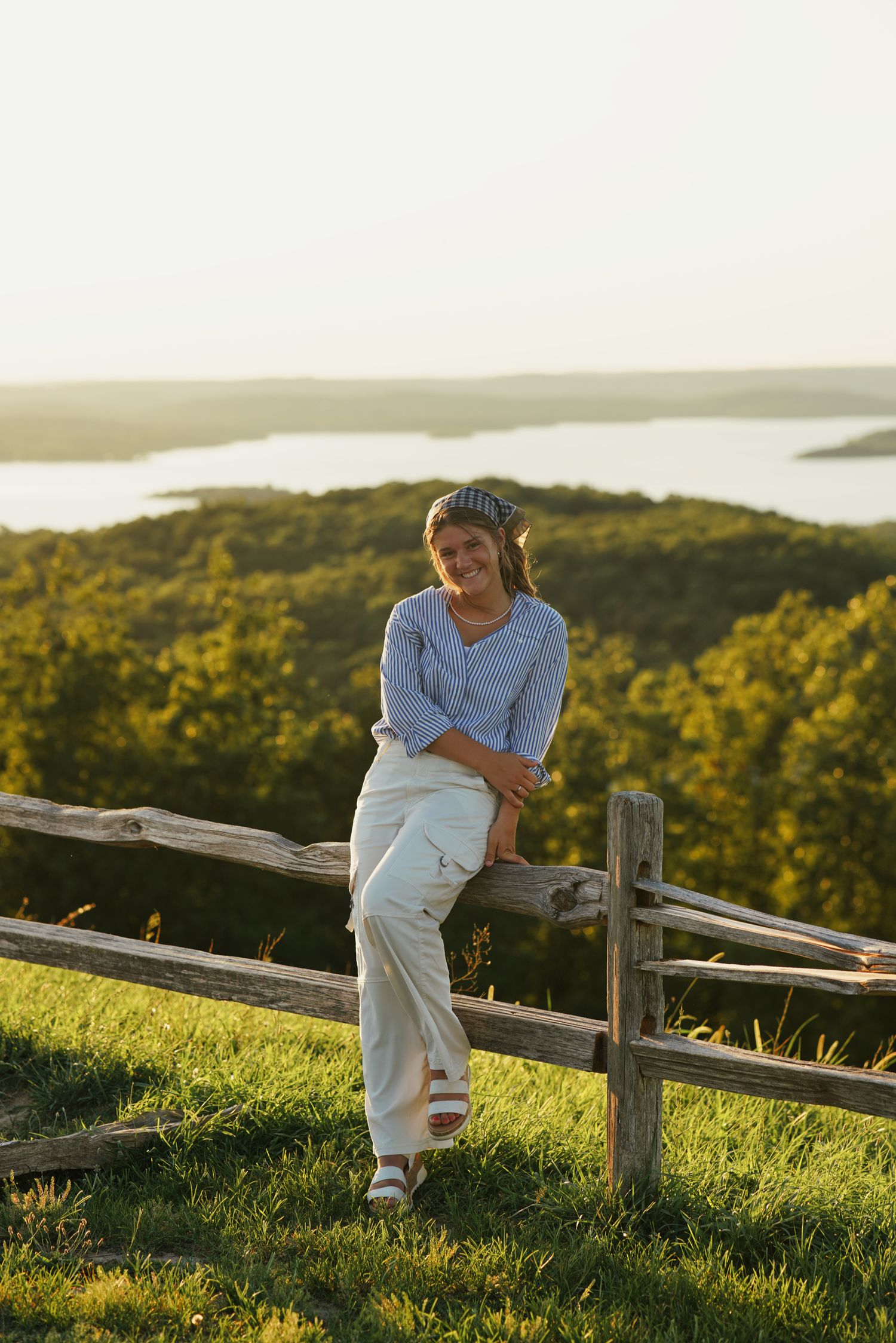 Senior portrait at sunset overlooking calm lake with warm golden light