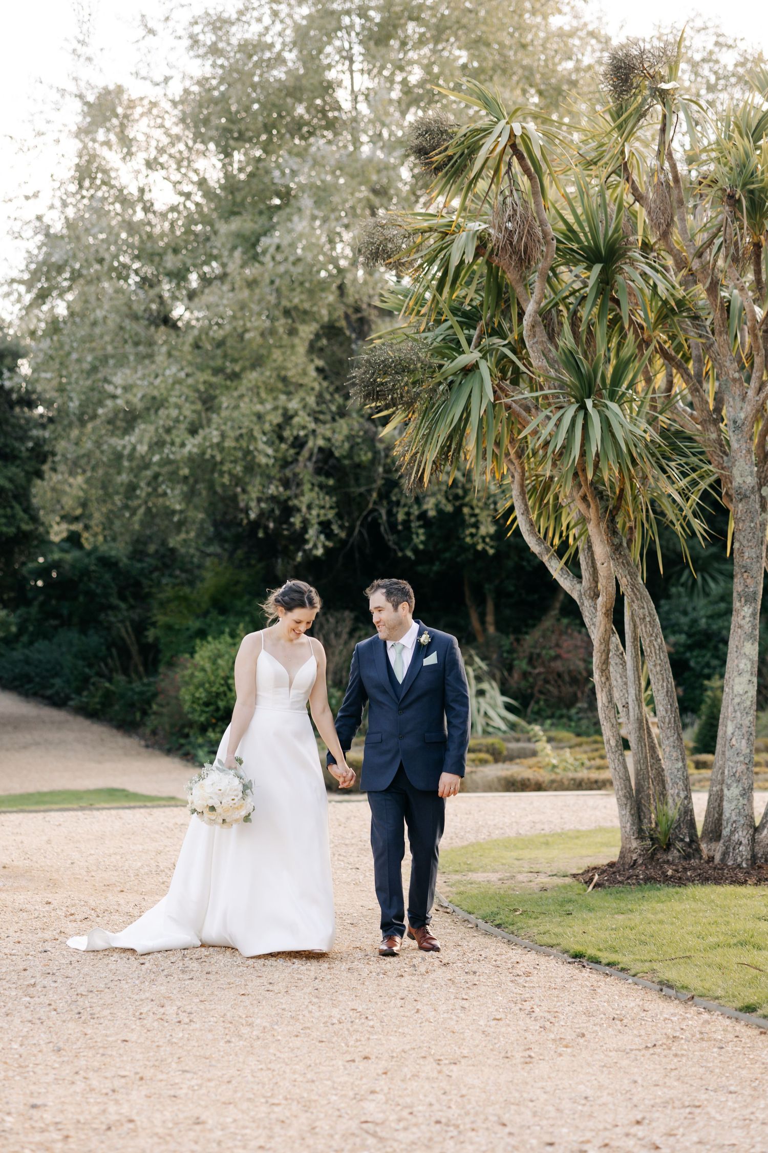 A couple walks along a sandy path lined with palm trees on their wedding day in a romantic outdoor setting.