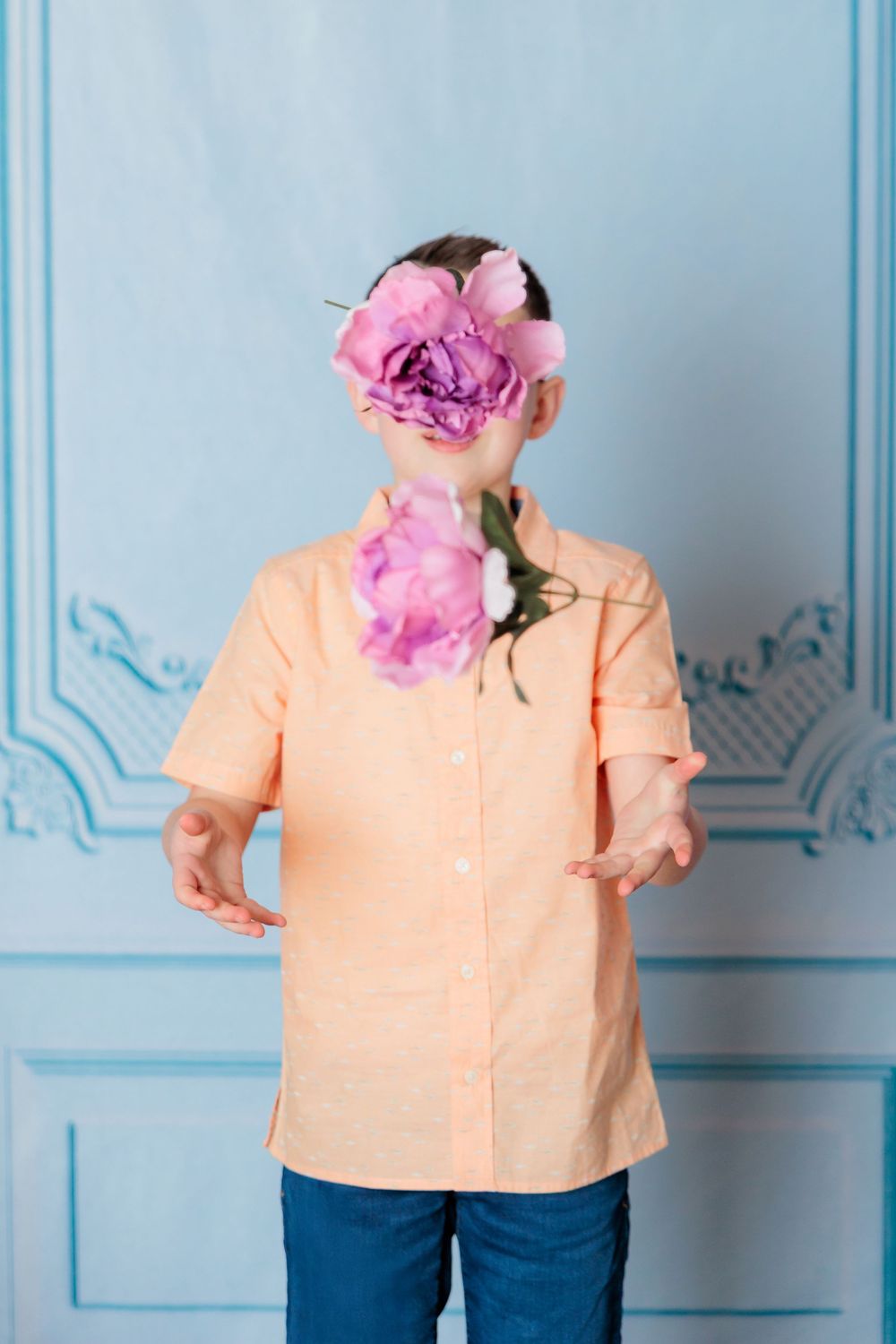 Creative portrait composition with pink roses obscuring figure in peach shirt against blue wall with decorative molding.
