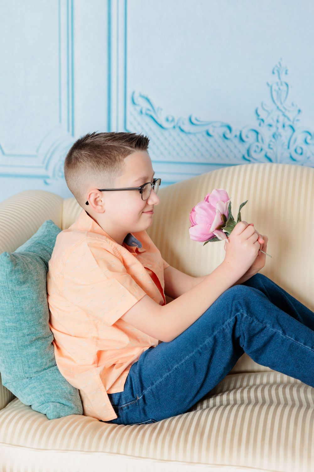 Person lounges comfortably on vintage sofa with teal pillows while reading in bright room.