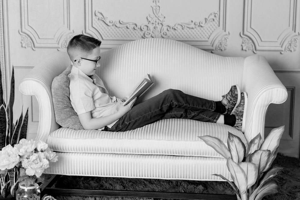 Black and white photos of a child resting on a white couch with decorative wall molding in background.