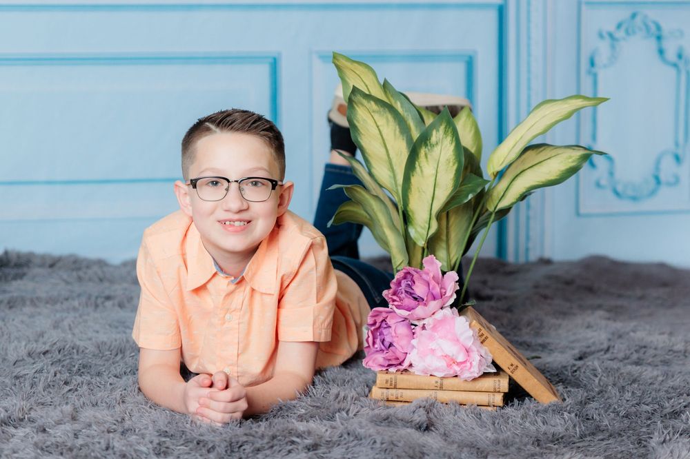 A person wearing a peach colored shirt lies on a gray carpet next to books and pink flowers.