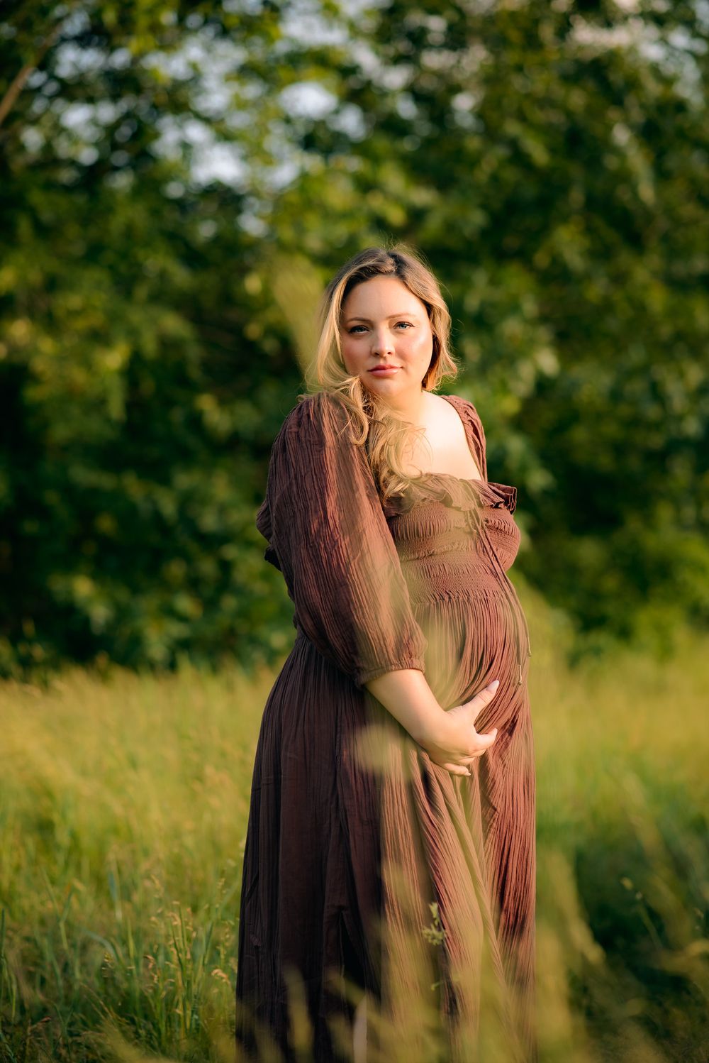 pregnant mama standing in golden lit meadow proudly showing off her pregnant belly