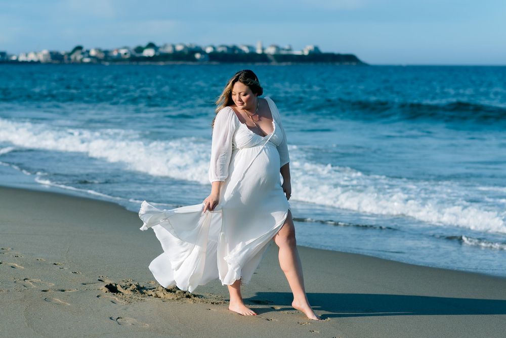 pregnant mother in flowing dress standing on an ocean beach during outdoor maternity session