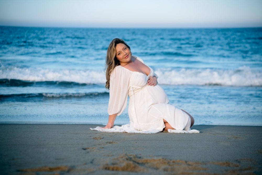 pregnant mom sitting on the beach with an ocean backdrop, posing for her maternity photoshoot