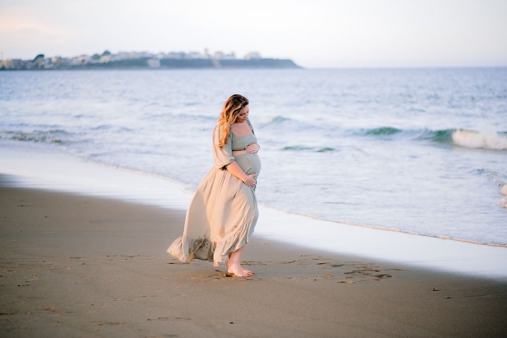 pregnant mother in flowing dress standing on the ocean beach for maternity session