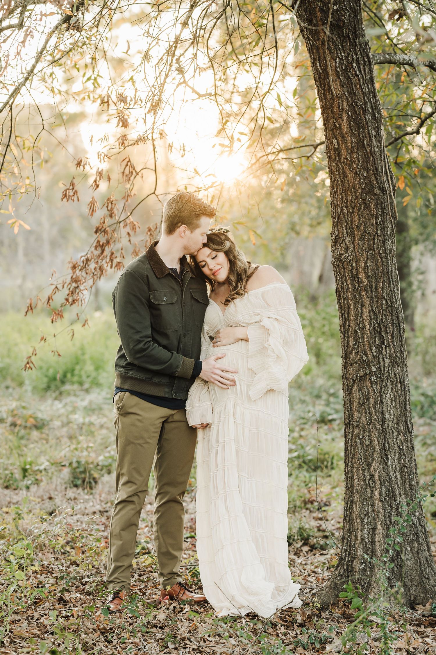 A romantic couple shares tender moments in a sunlit forest setting wearing white and olive green outfits for houston maternity photographer