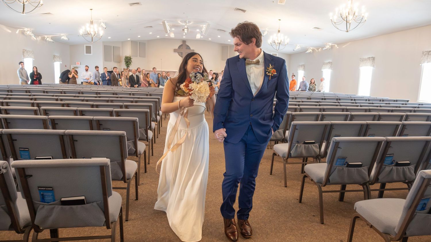 A panoramic view of a church interior with pews and elegant white decor during a wedding ceremony.