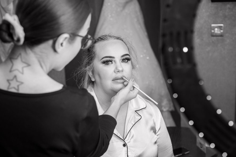 Black and white photo of a makeup artist applying lipstick to a bride before her wedding.