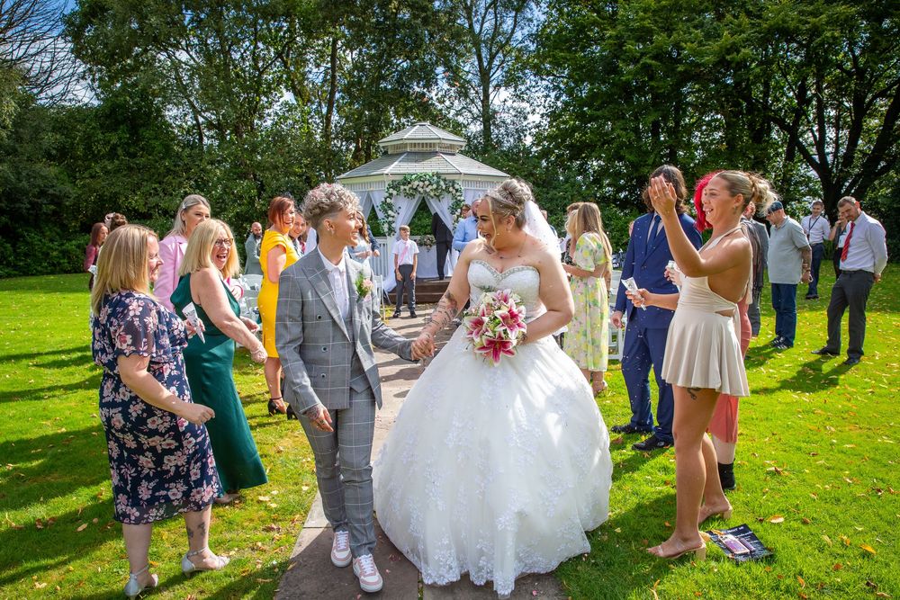 Newlywed couple celebrating with guests on garden path after outdoor wedding ceremony.