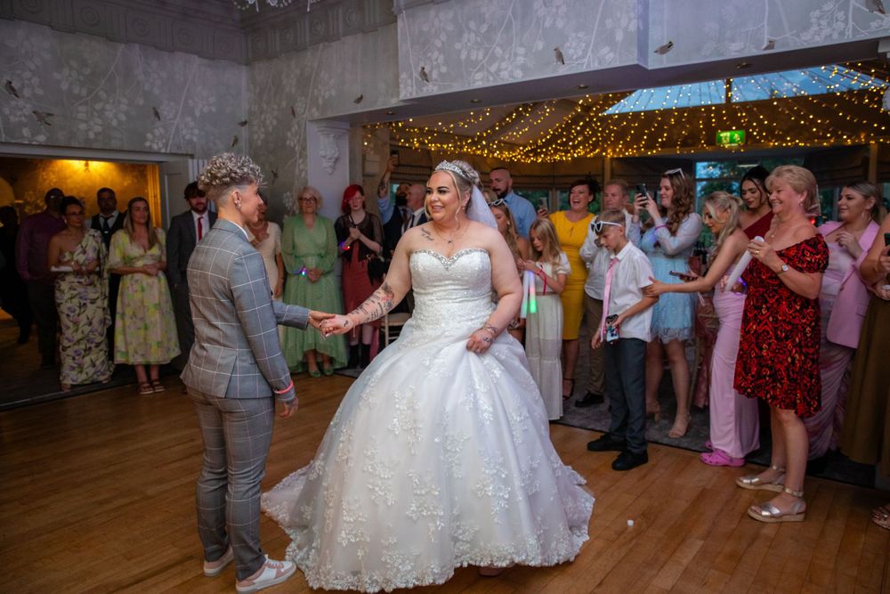 Bride and groom sharing first dance surrounded by cheering guests at elegant wedding reception.