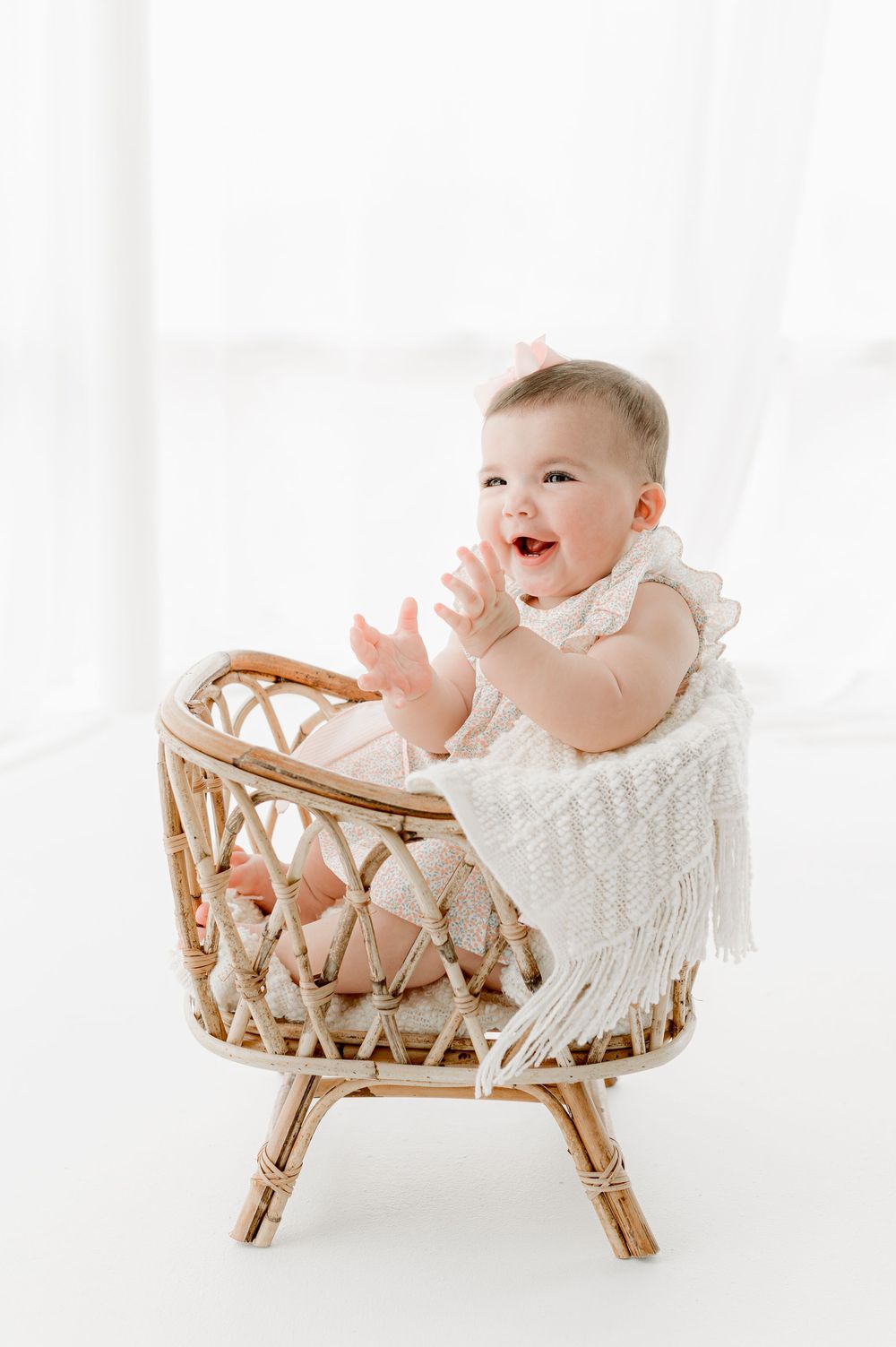 A happy baby wearing white sits in a woven rattan basket against a bright white background.